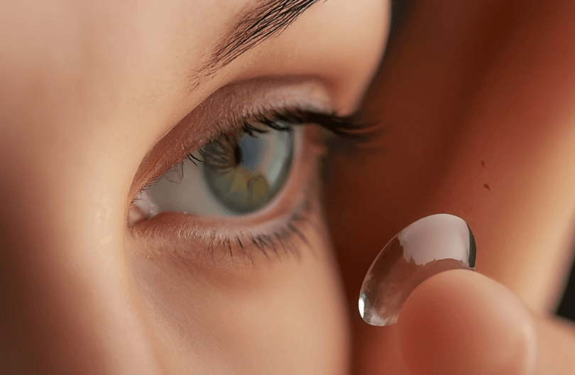 A close-up of an individual preparing to insert a clear contact lens into their eye.